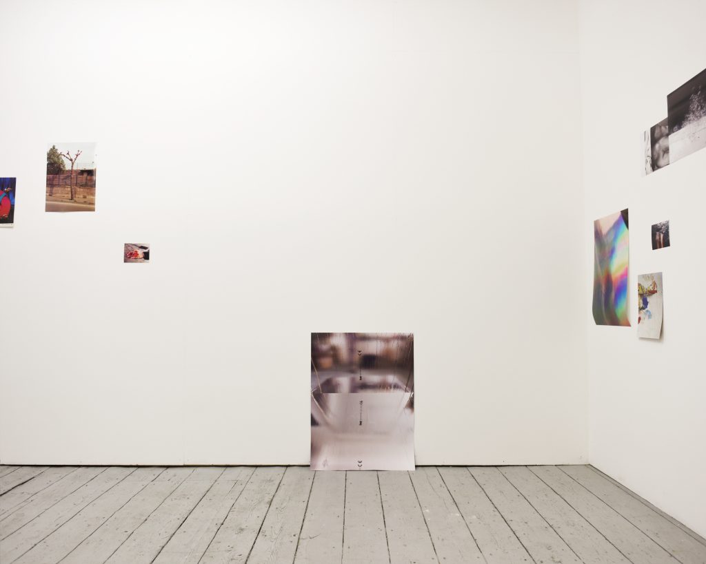 Exhibition installation shot, showing one wall and the wooden floor of the gallery. A large photograph which is an image of a reflective plasterboard surface faces the viewer and is attached low to the wall so that the bottom touches the floor.