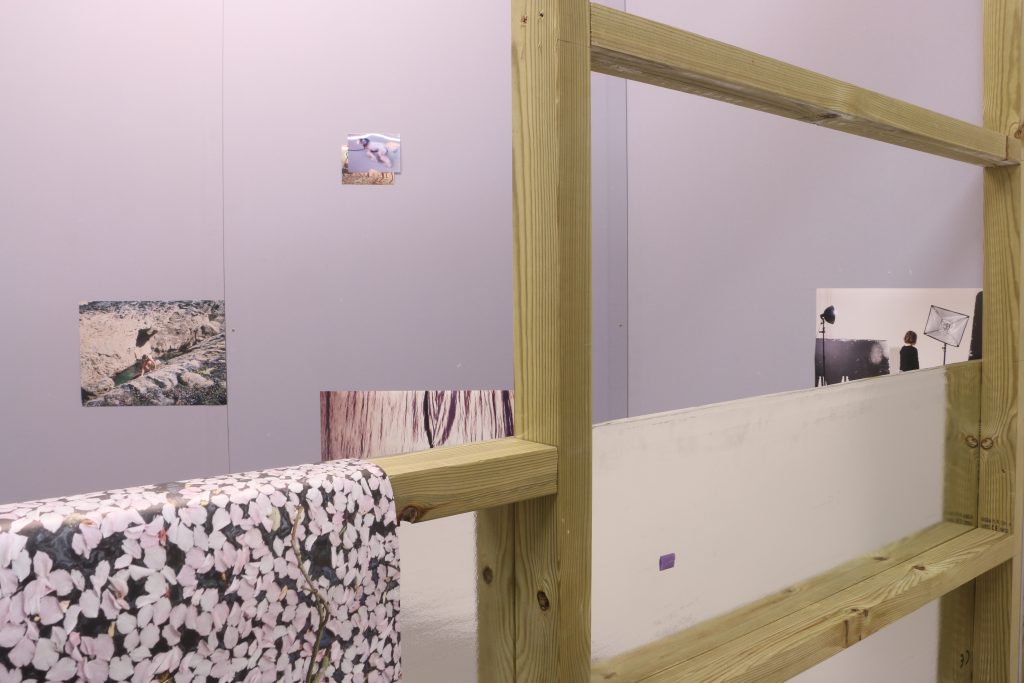 Installation shot showing a detail of the exhibition - wooden bars through which you can see photographs, in this image the detail is unclear of each photograph but there is a sense of different materials and pattern.