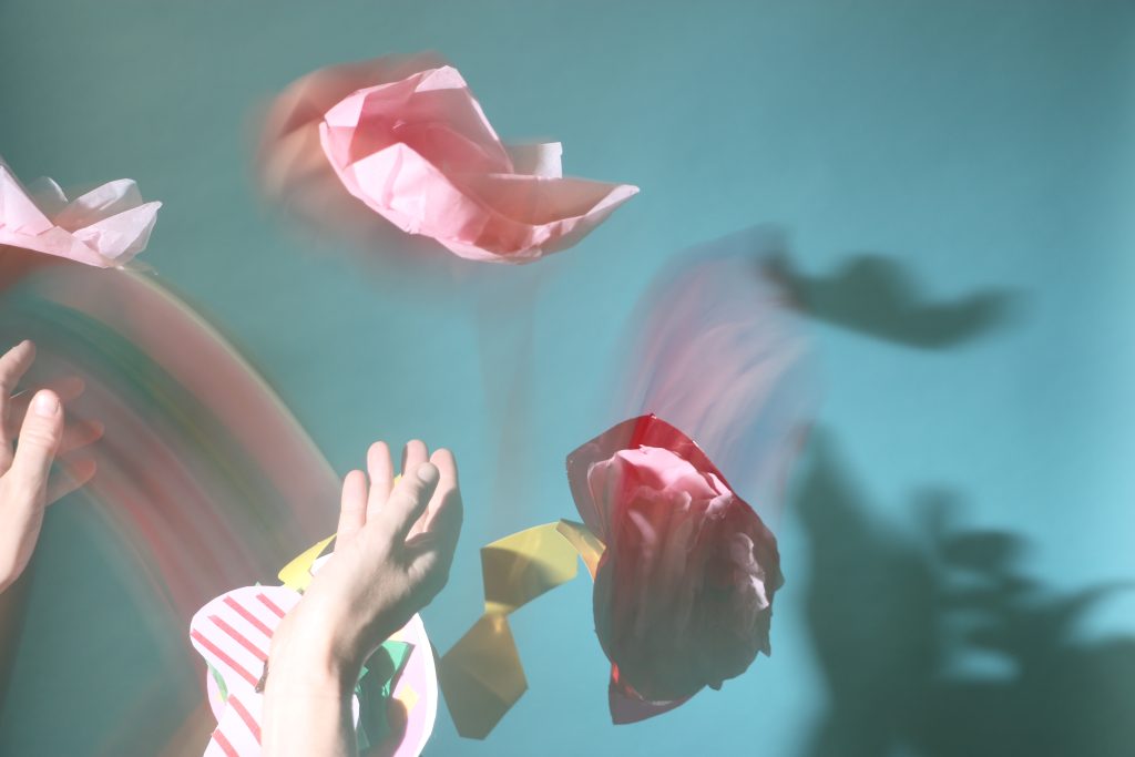 Photograph of hands throwing paper flowers in the air.