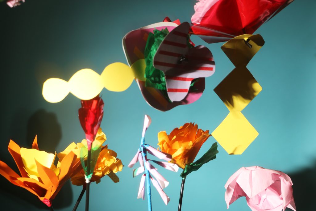 Photograph of coloured paper flowers thrown in the air. Flash photography.