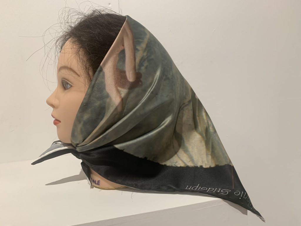 White background, hairdressing model's head of white woman with dark hair. Hair wrapped in headscarf featuring photographic print of hand.