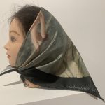 White background, hairdressing model's head of white woman with dark hair. Hair wrapped in headscarf featuring photographic print of hand.