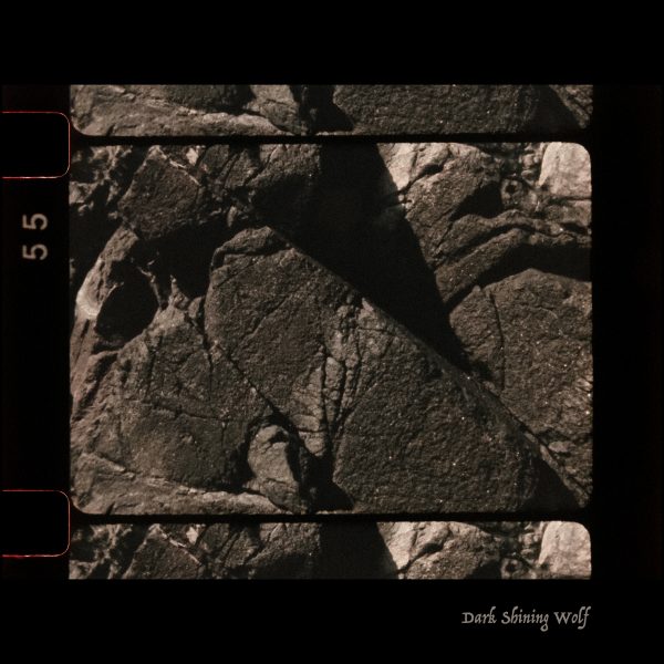 Square photographic image with black border, shows dark rocks with angular shadows.