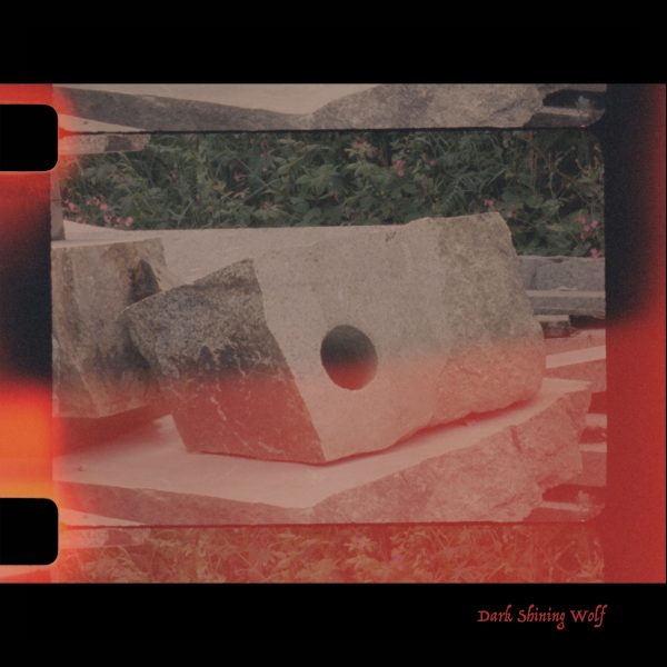 Square photographic image with black border. Still from a 16mm film - orange light leeks visible on the bottom half of the image. Image is of a piece of stone with a carved hole on the left hand side.