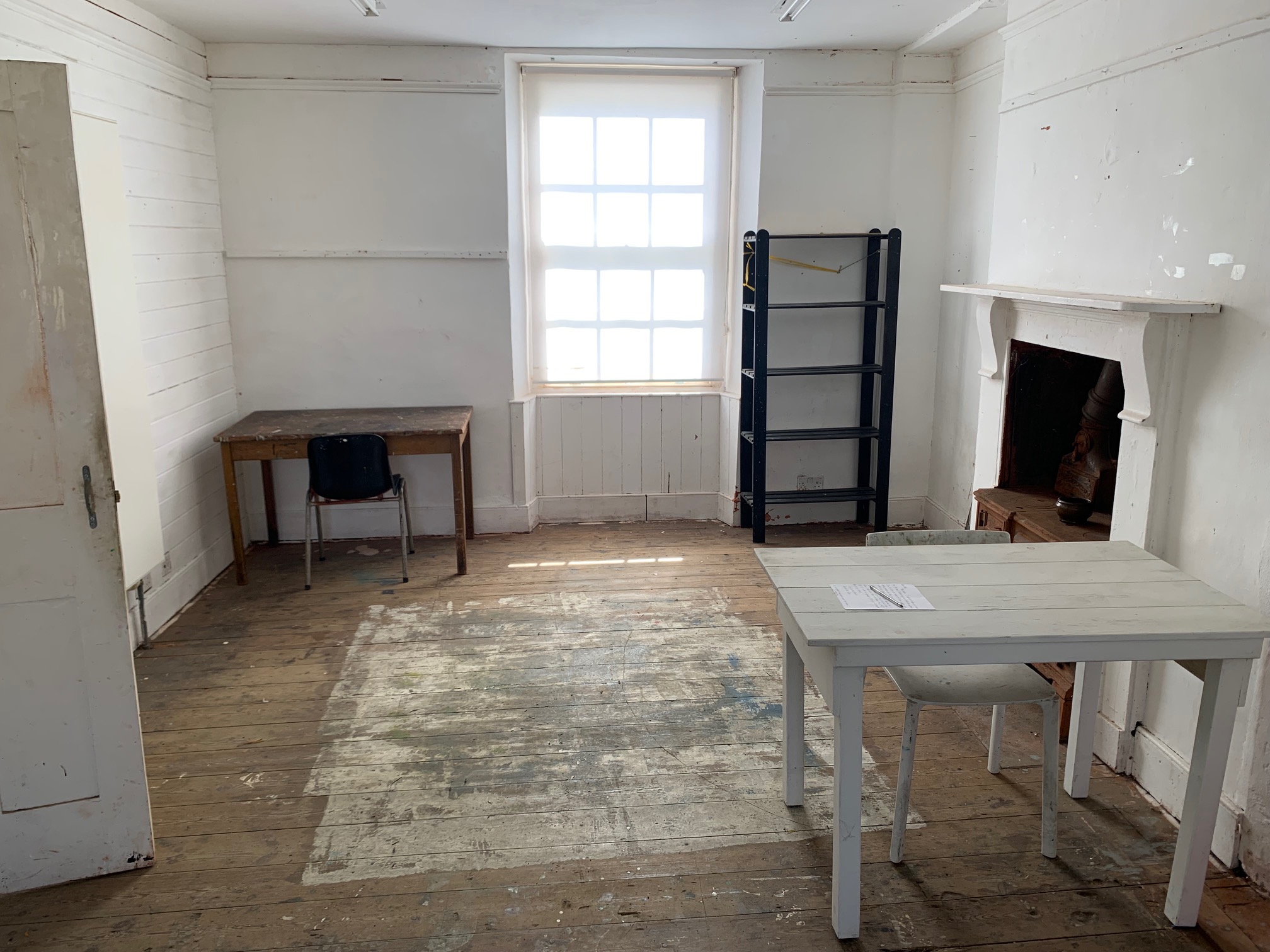 Photograph of a room with wooden floor and white walls. A studio.
